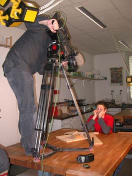 Foto der Dreharbeiten. Auf der Werkbank steht ein Kameramann mit Stativ und Kamera. Ich sitze am Tisch mit Holzproben